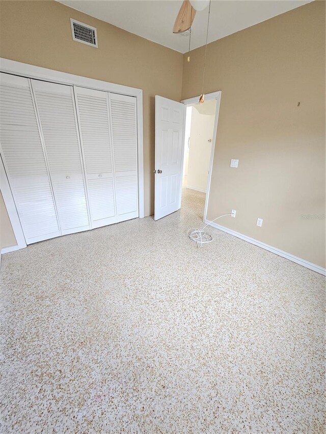 unfurnished bedroom with baseboards, visible vents, ceiling fan, speckled floor, and a closet