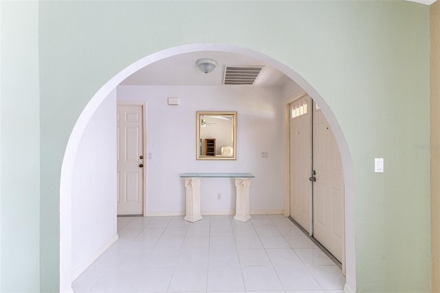 corridor with light tile patterned floors, baseboards, visible vents, and arched walkways