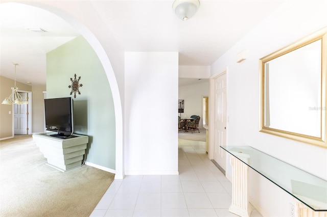 hall with light carpet, light tile patterned floors, arched walkways, and baseboards