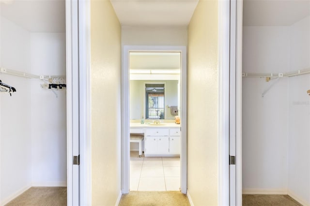 hall featuring light tile patterned floors, baseboards, a sink, and light colored carpet