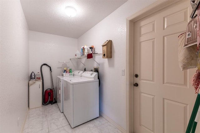 clothes washing area with laundry area, baseboards, marble finish floor, a textured ceiling, and washer and dryer