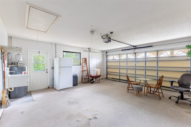 garage featuring water heater, a garage door opener, a sink, and freestanding refrigerator