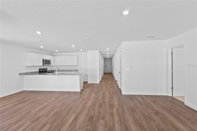 kitchen with a peninsula, wood finished floors, white cabinetry, open floor plan, and appliances with stainless steel finishes