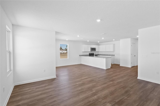 unfurnished living room featuring baseboards, dark wood finished floors, a textured ceiling, and recessed lighting