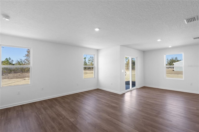 unfurnished room featuring dark wood-style floors, visible vents, a textured ceiling, and baseboards