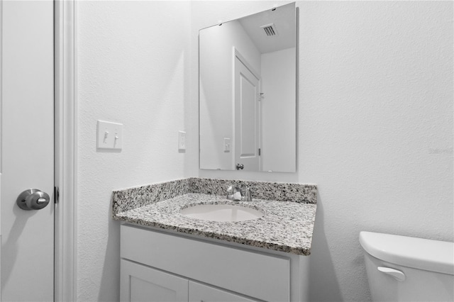 bathroom with toilet, a textured wall, visible vents, and vanity