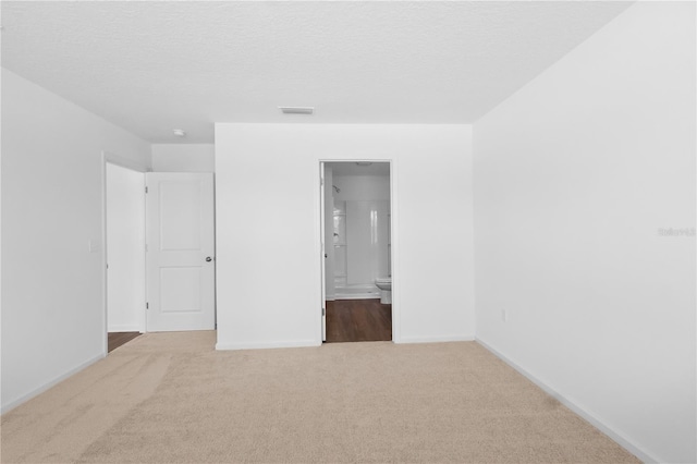 unfurnished bedroom featuring a textured ceiling, ensuite bathroom, carpet flooring, visible vents, and baseboards