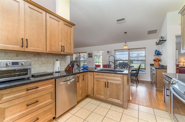 kitchen featuring a peninsula, appliances with stainless steel finishes, a sink, and visible vents