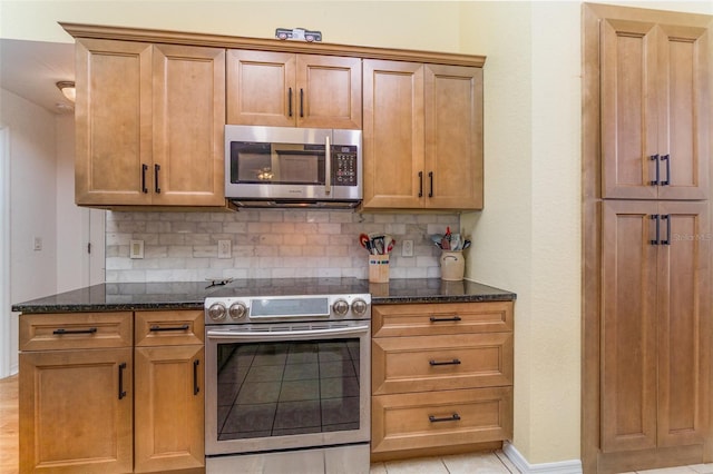 kitchen featuring appliances with stainless steel finishes, baseboards, dark stone countertops, and tasteful backsplash