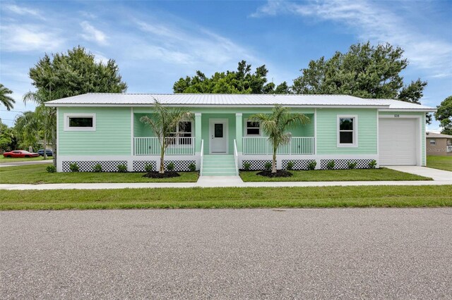 view of front facade featuring covered porch, concrete driveway, metal roof, a garage, and a front lawn