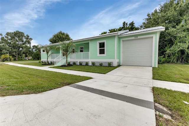 ranch-style house featuring metal roof, an attached garage, covered porch, concrete driveway, and a front lawn