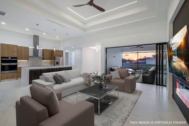 living area with a raised ceiling, a ceiling fan, and visible vents