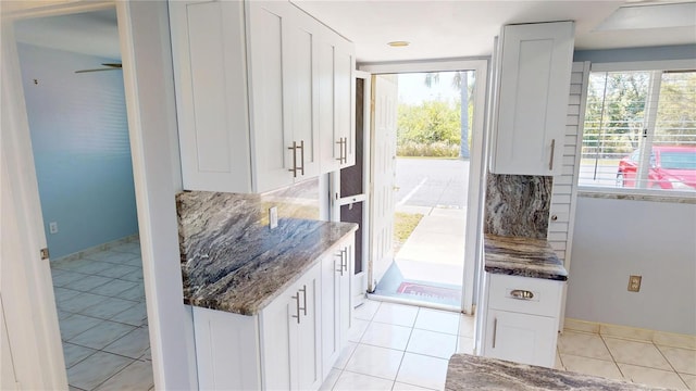 kitchen featuring light tile patterned floors, white cabinetry, dark stone counters, and decorative backsplash