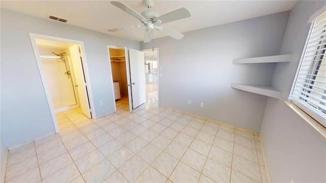 unfurnished bedroom featuring a walk in closet, a closet, visible vents, light tile patterned flooring, and ceiling fan