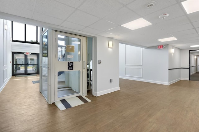 interior space featuring a drop ceiling, baseboards, and wood finished floors