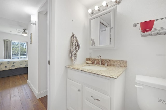 bathroom with toilet, a ceiling fan, hardwood / wood-style floors, connected bathroom, and vanity