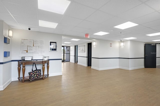 interior space with a drop ceiling, baseboards, and wood finished floors