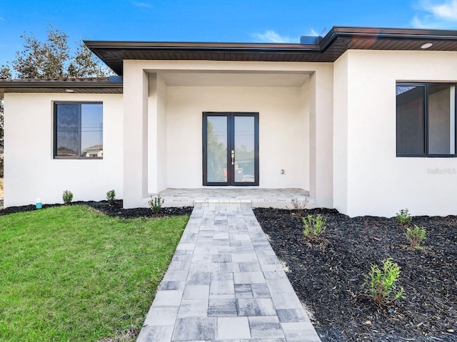 view of exterior entry featuring a yard, french doors, and stucco siding