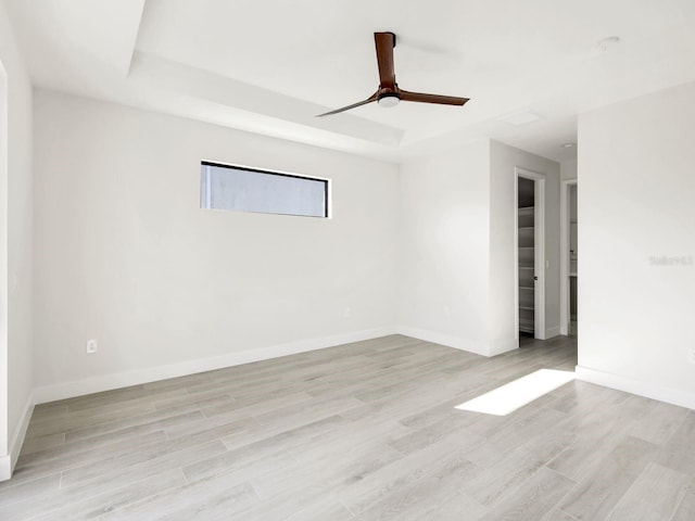 spare room featuring a tray ceiling, baseboards, and light wood finished floors