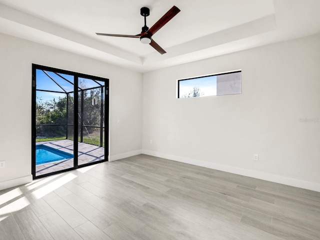 empty room with light wood finished floors, plenty of natural light, and a raised ceiling