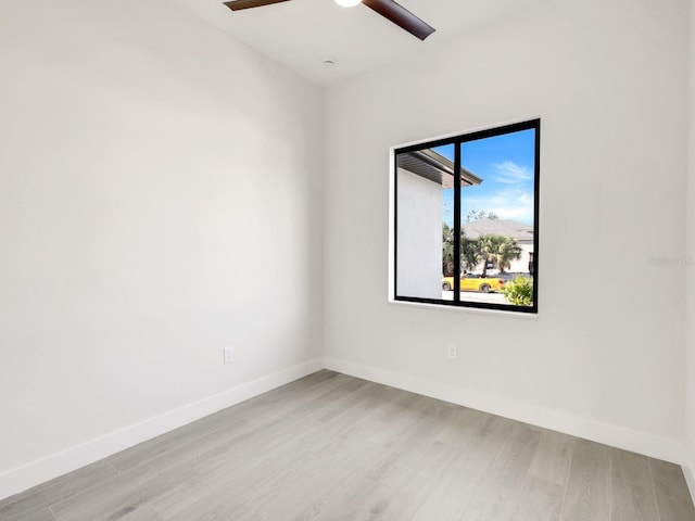 spare room featuring light wood finished floors, a ceiling fan, and baseboards