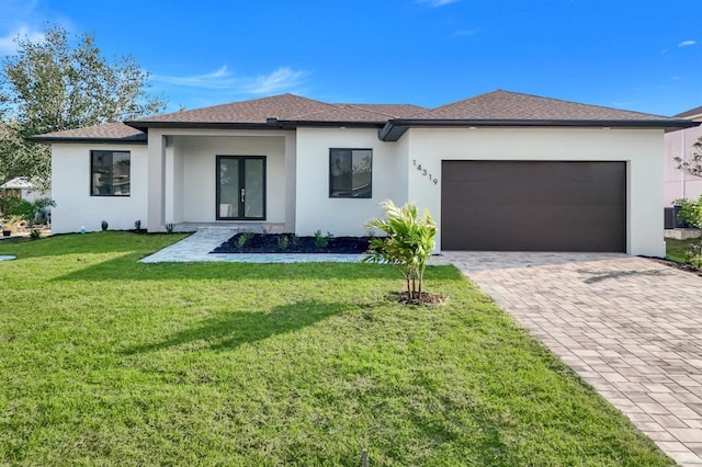 prairie-style home with decorative driveway, french doors, stucco siding, an attached garage, and a front lawn