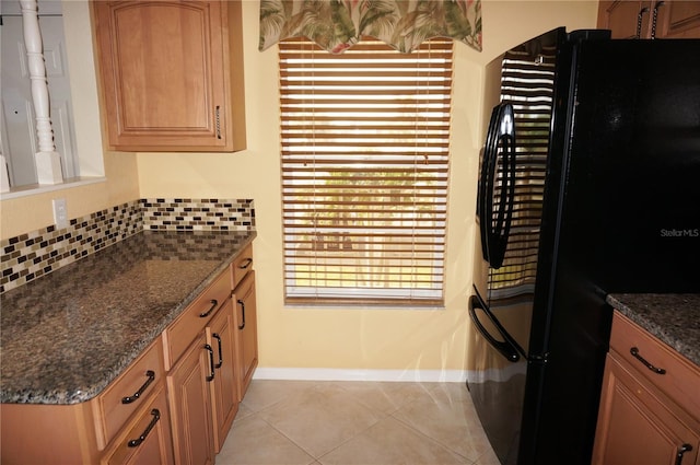 kitchen featuring light tile patterned flooring, dark stone countertops, backsplash, and freestanding refrigerator