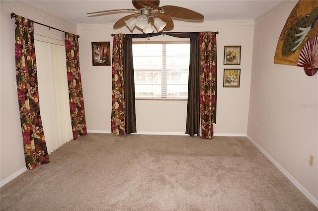 carpeted spare room with ornamental molding, a ceiling fan, and baseboards