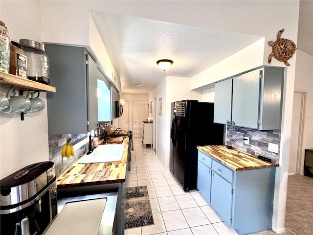 kitchen with light tile patterned floors, butcher block counters, freestanding refrigerator, and decorative backsplash