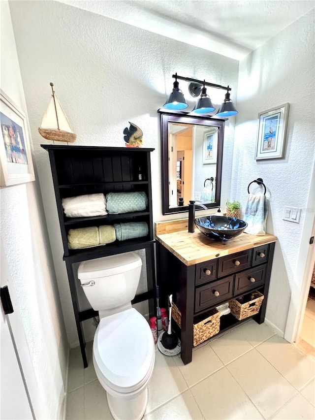 half bath with baseboards, a textured wall, toilet, tile patterned flooring, and vanity