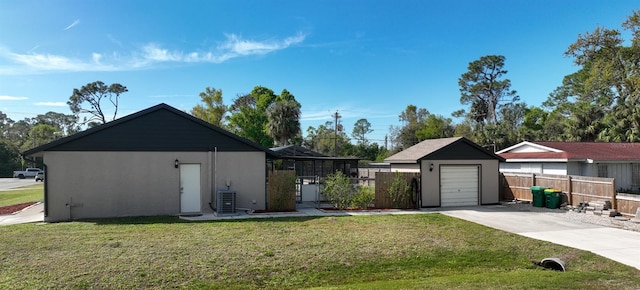 view of yard with an outbuilding, a detached garage, concrete driveway, central AC, and fence