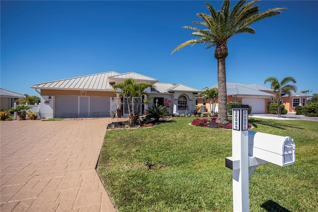 ranch-style house with a front yard, metal roof, decorative driveway, an attached garage, and a standing seam roof