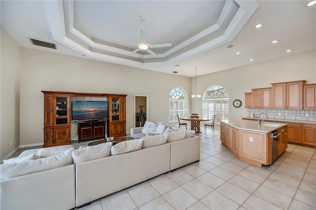 living area with visible vents, ceiling fan with notable chandelier, a tray ceiling, and ornamental molding