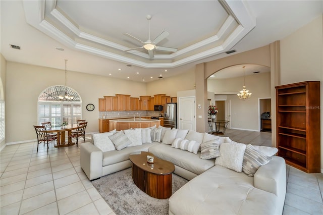 living room with a tray ceiling, arched walkways, visible vents, and crown molding