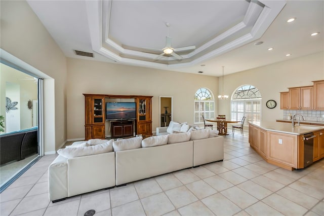 living room with visible vents, ceiling fan with notable chandelier, a tray ceiling, light tile patterned flooring, and crown molding