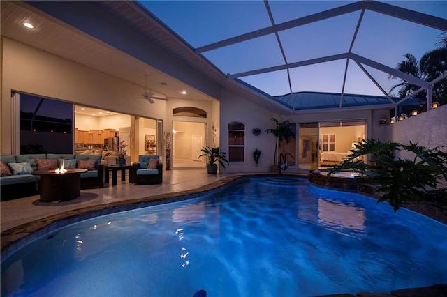 view of swimming pool featuring a ceiling fan, a pool with connected hot tub, glass enclosure, an outdoor living space with a fire pit, and a patio area