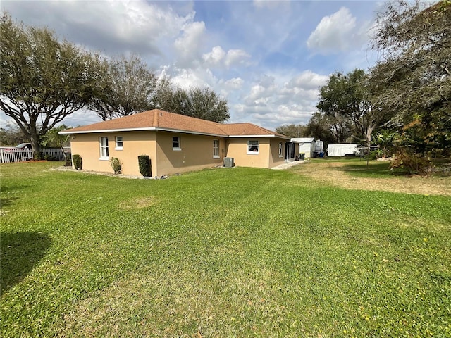 rear view of property with a yard, central air condition unit, fence, and stucco siding