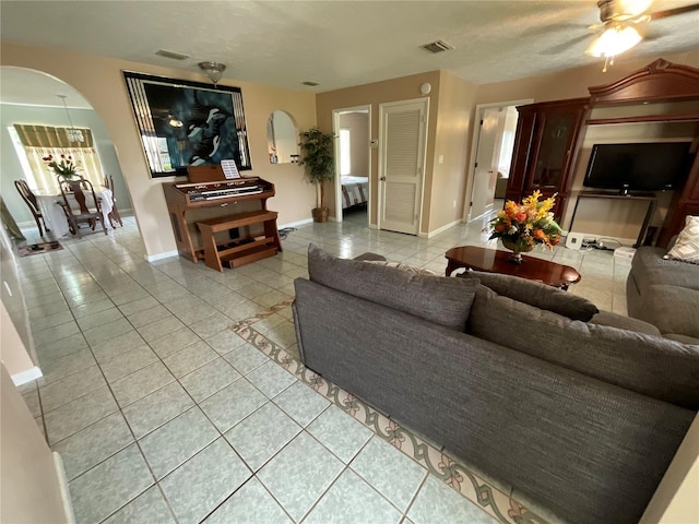 living room featuring light tile patterned floors, baseboards, visible vents, and arched walkways