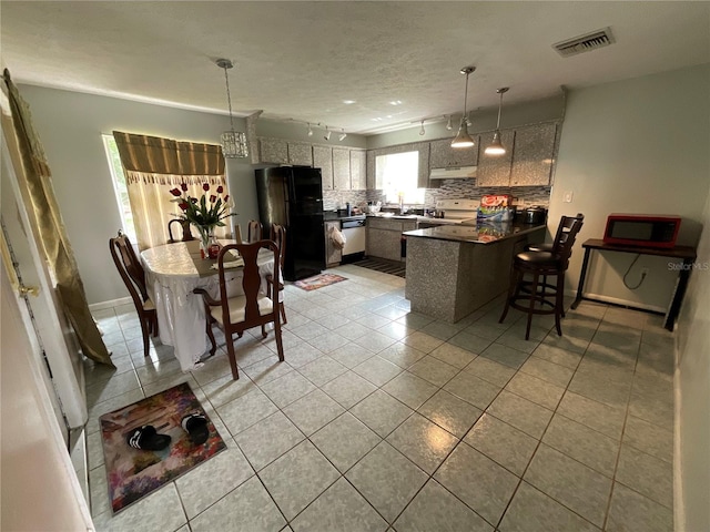 kitchen featuring visible vents, dark countertops, freestanding refrigerator, a peninsula, and under cabinet range hood