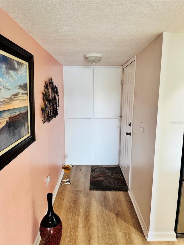 hall with a textured ceiling, baseboards, and wood finished floors