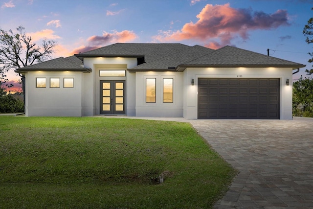 prairie-style house featuring a garage, a yard, french doors, decorative driveway, and stucco siding