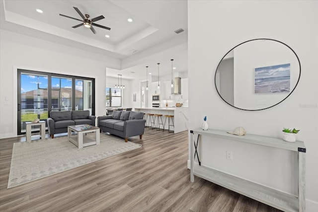 living area featuring visible vents, a ceiling fan, wood finished floors, a tray ceiling, and recessed lighting