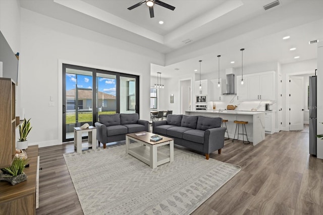 living area with baseboards, visible vents, a tray ceiling, and wood finished floors