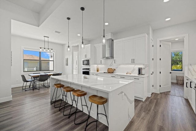 kitchen with a kitchen island, appliances with stainless steel finishes, dark wood-style flooring, wall chimney range hood, and white cabinetry