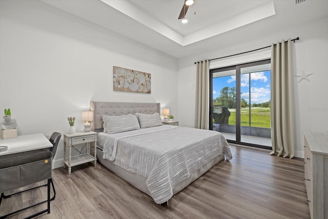 bedroom featuring ceiling fan, wood finished floors, baseboards, access to outside, and a raised ceiling