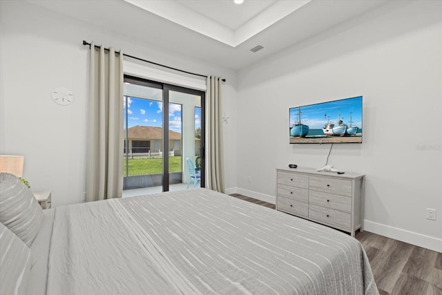 bedroom with access to exterior, a tray ceiling, visible vents, wood finished floors, and baseboards