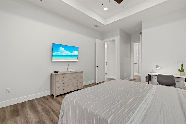 bedroom featuring recessed lighting, wood finished floors, a ceiling fan, baseboards, and a tray ceiling