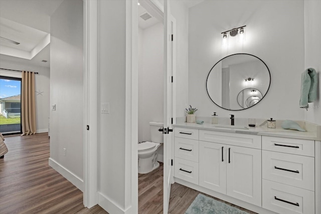 bathroom with visible vents, toilet, vanity, wood finished floors, and baseboards