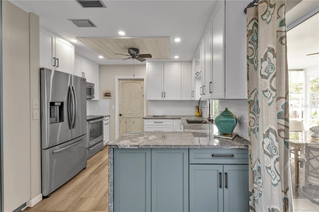 kitchen with visible vents, appliances with stainless steel finishes, light stone counters, a peninsula, and light wood-type flooring