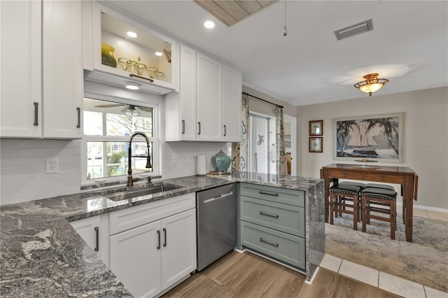 kitchen featuring dark stone counters, a peninsula, stainless steel dishwasher, white cabinetry, and a sink